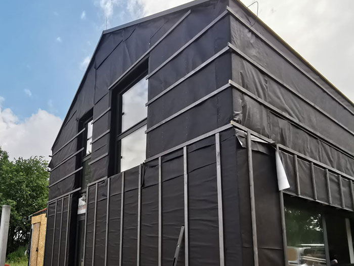 Haus mit schwarzer Fassade und großen Fenstern.